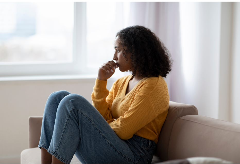 Young woman sitting on sofa looking sadly into the distance. 