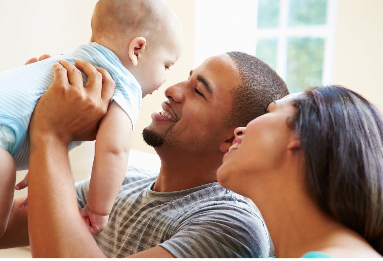 Dad holding up baby while mom looks lovingly at baby.