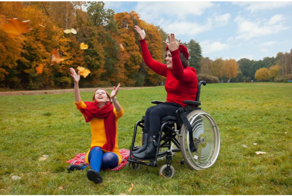 Person in wheelchair and person sitting on the ground catching the Fall leaves. 