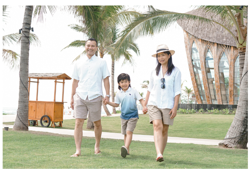 Father, son, and mother holding hands and walking in a tropical location.