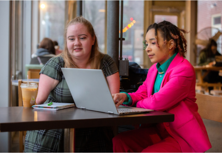 Young woman getting help from a woman typing on a laptop. 